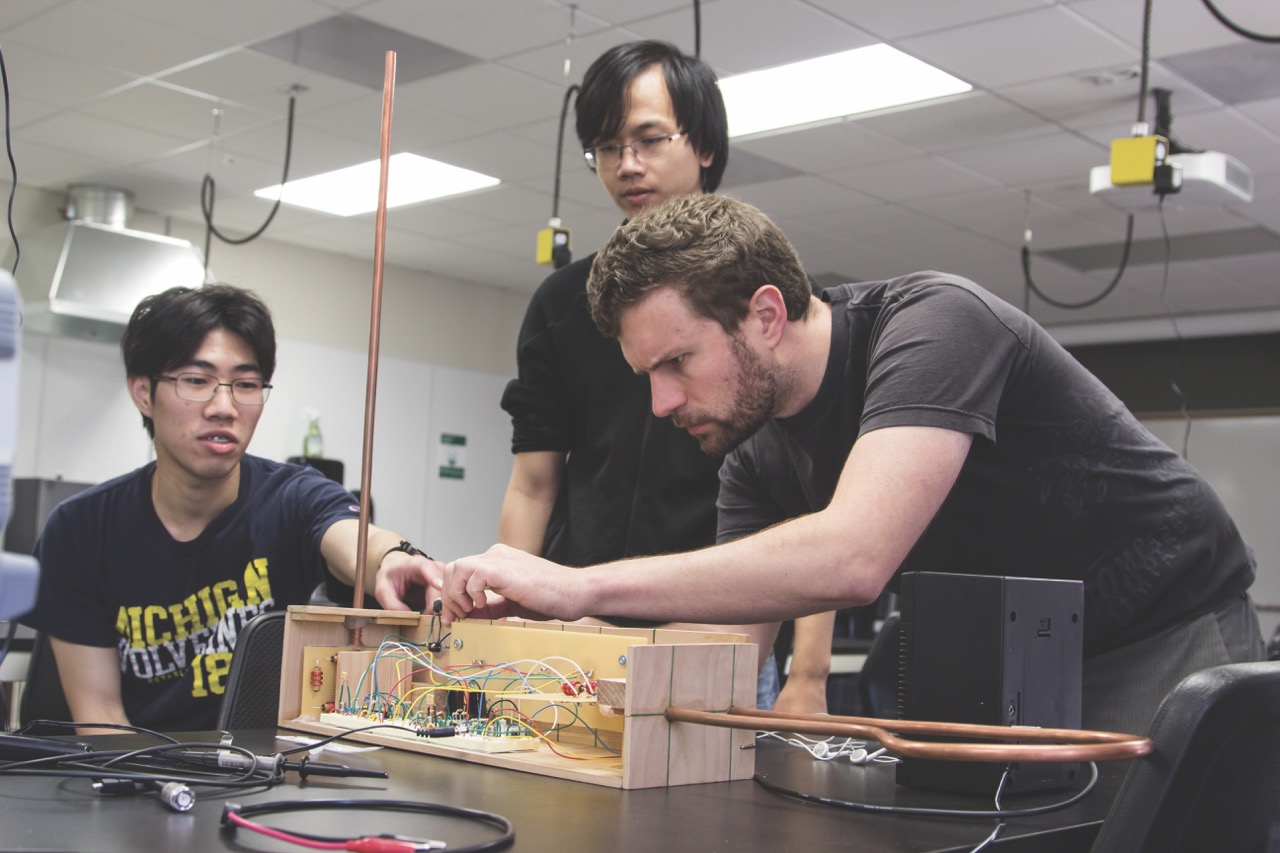 Studentswearing black shirts working on a wooden prototype inside a lab 