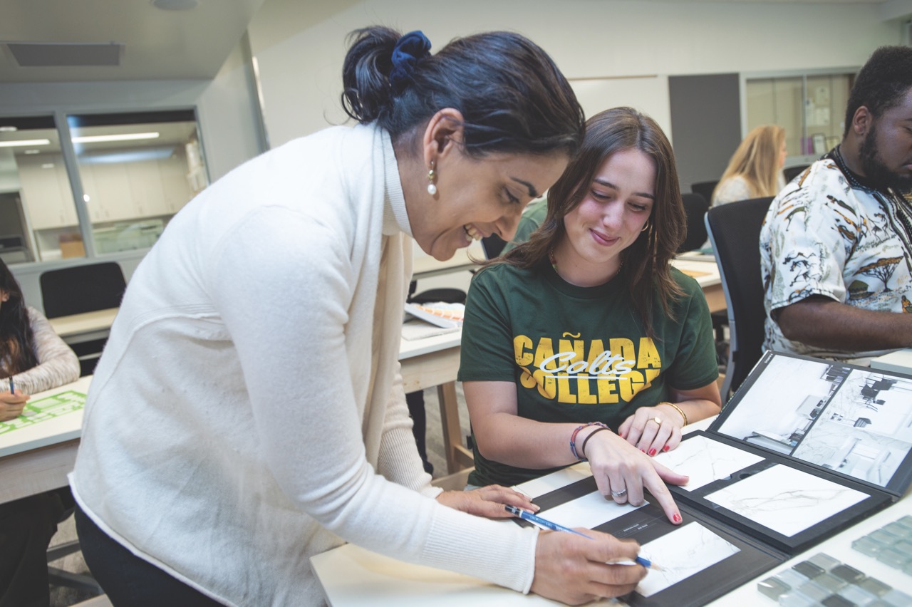 A student wearing a green shirt signaling on a table next to a professor