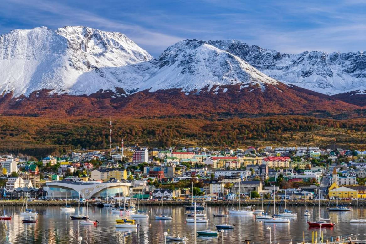 boats in a harbor town set in front of snowy mountains