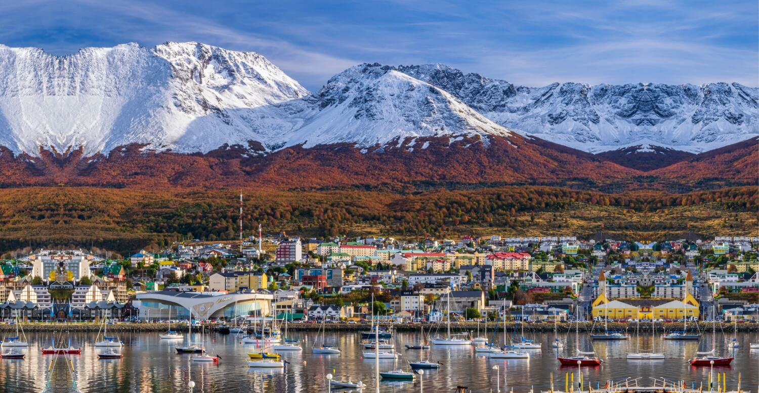 Snowy mountains behind a coastal city in Argentina, with many sailboats in the harbor