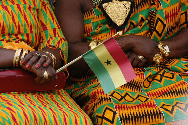 hands holding a Ghana flag and dressed in bright traditional clothes