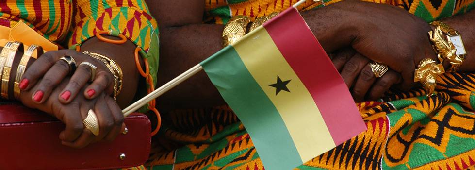 women in brightly colored clothing hold the flag of Ghana